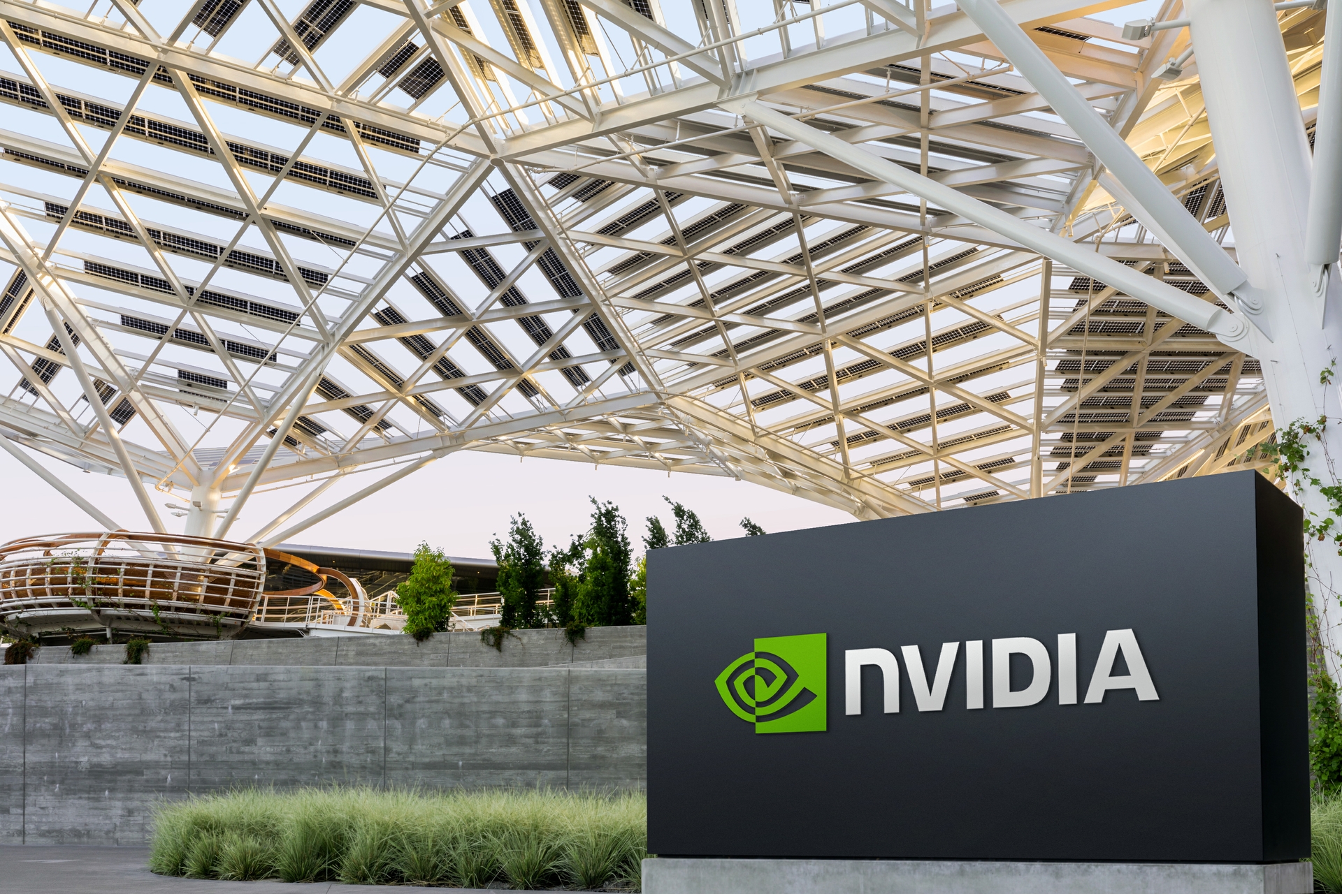 흰 철골 구조 지붕 아래 녹색 로고가 있는 검은 NVIDIA 간판이 서 있는 엔비디아 본사 입구